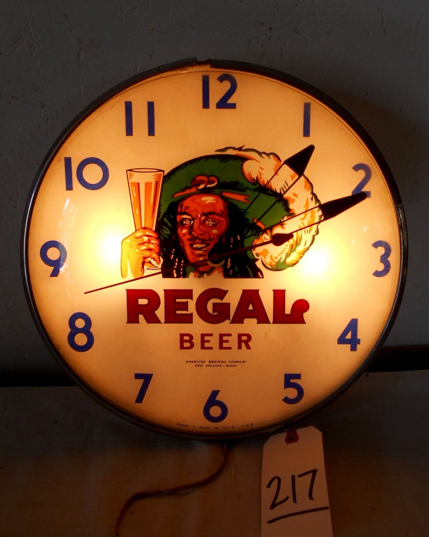 REGAL BEER Clock: Vintage REGAL BEER advertisement wall clock with metal housing and glass front. Metal framing band is coming off in one spot. Has numbers 6 77 on back. Possibly the date? Clock runs and lights up. 15"