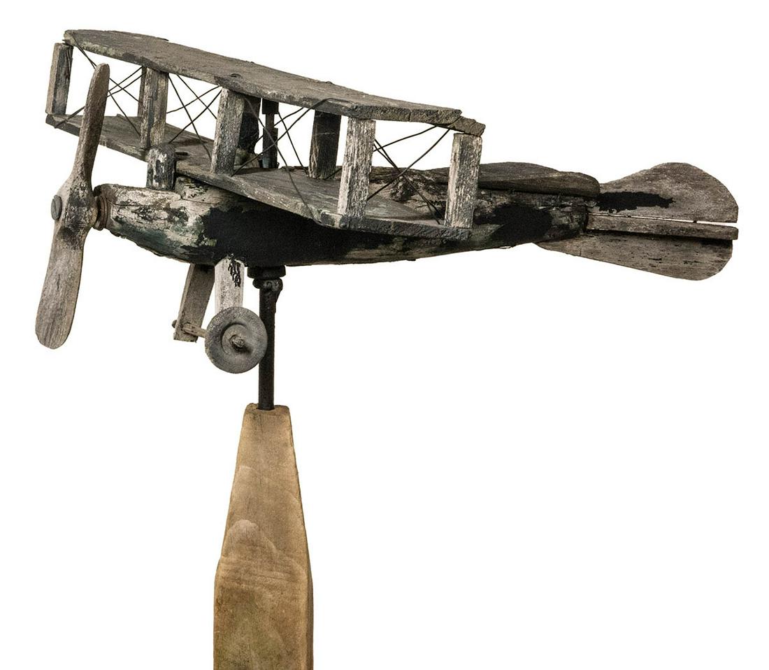 EARLY 20TH C. BIPLANE WEATHERVANEPrimitive, pine,: EARLY 20TH C. BIPLANE WEATHERVANEPrimitive, pine, bi-plane weathervane, old black weathered paint, pilot in cockpit, one wheel missing, on stand, 16" l.