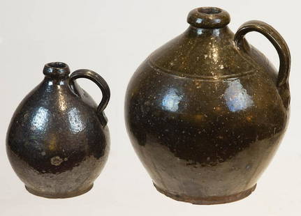 TWO EARLY REDWARE OVOID JUGSBoth jugs with dark: TWO EARLY REDWARE OVOID JUGSBoth jugs with dark manganese glaze, large 10" h jug with grooved handle, 9" w; Smaller 6 1/2" h jug with grooved handle, small kiln check on midbody, otherwise good