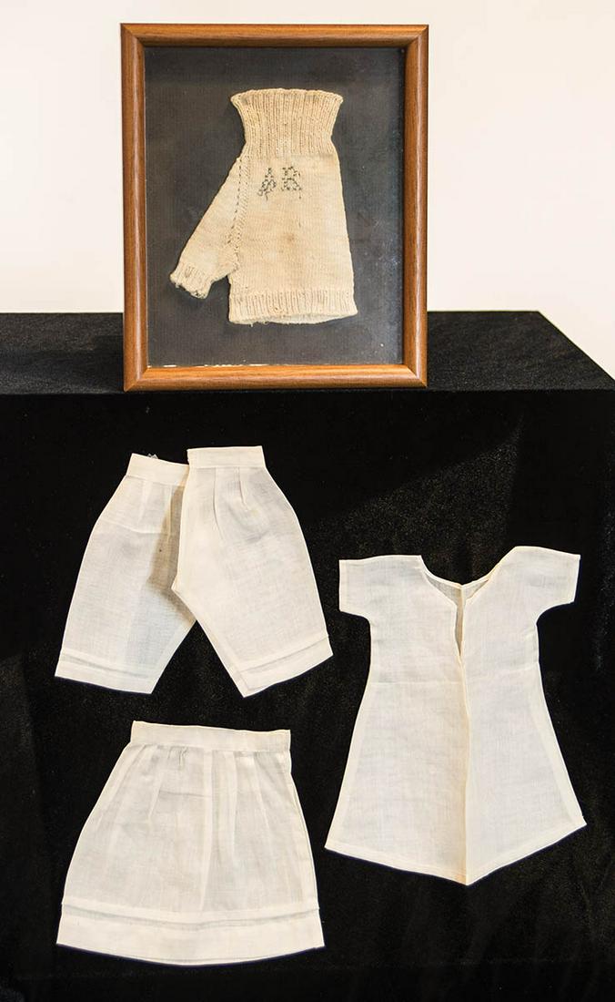 SISTER'S GLOVE AND DOLL CLOTHINGFramed white wool, stitch initialed in blue "AR", along with pieces: SISTER'S GLOVE AND DOLL CLOTHINGFramed white wool, stitch initialed in blue "AR", along with pieces of doll undergarments.