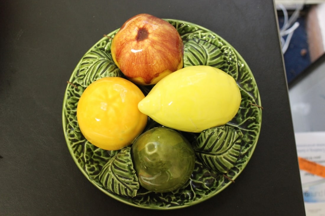 A Jay Willfred Fruit Plate Hanger: 3 Dimensional - Made in Portugal - 8 1/2" in diameter and 4" tall - Signed or labeled underneath the plate - please note: manufacturer imperfection on the lemon