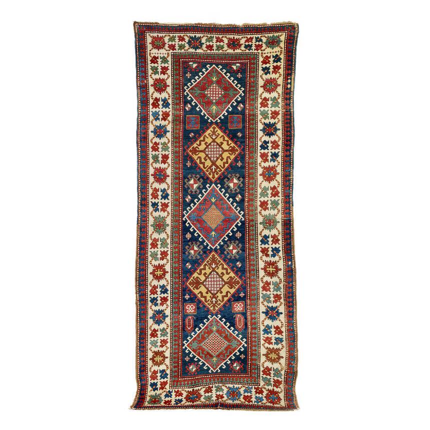 Kazak: Late 19th century, 343 x 144 cm, South West Caucasus Five large diamonds aligned on the central axis of the dark blue field each enclose a smaller diamond surrounded by abstract animals. The wide, whi
