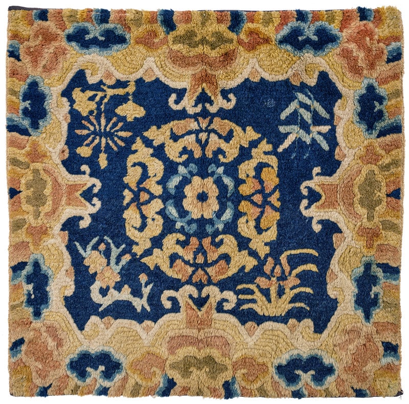 Ningxia Seat Cover: mid 19th century, 61 x 62 cm, West China In the dark blue field of this square seat cover, a floral disc medallion is surrounded by four flowering branches. A water-and-waves border with Mount Meru