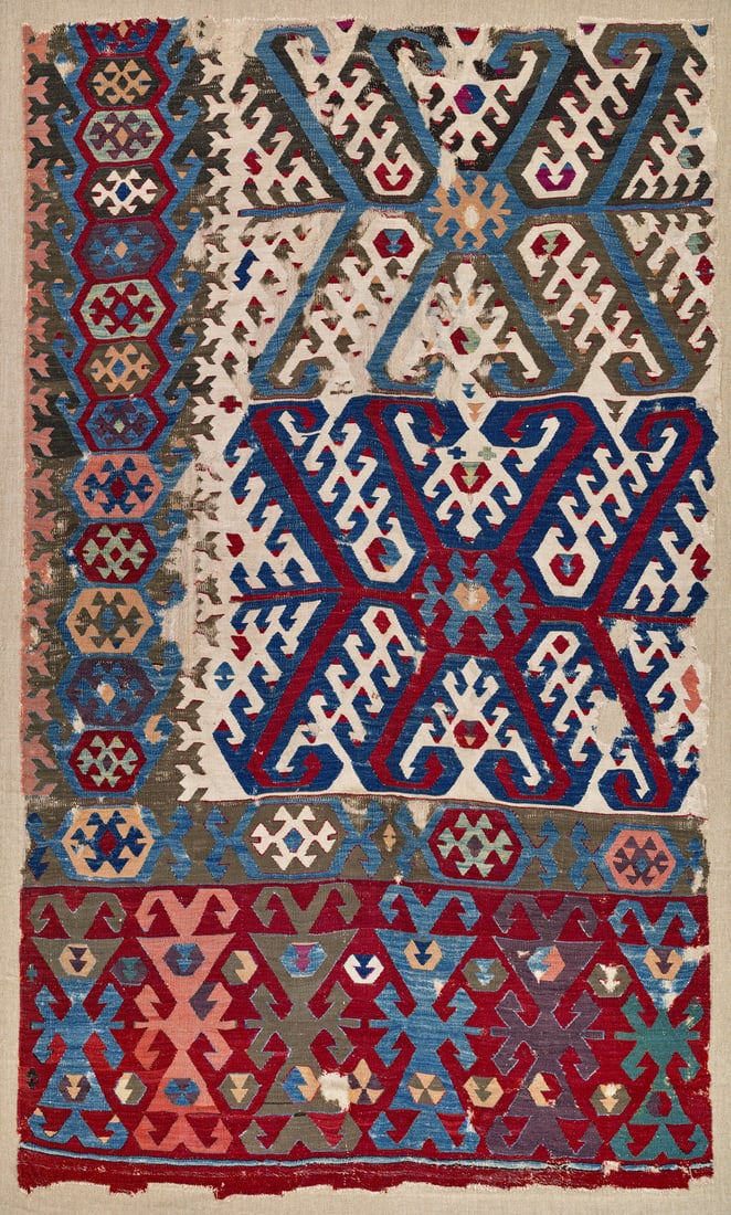 Hotamis Kilim Fragment: mid 19th century, 137 x 114 cm, Central Anatolia, Konya A corner section from one panel of a white-ground kilim. The earth-brown border contains hexagons. The wide red-ground elem displays six large