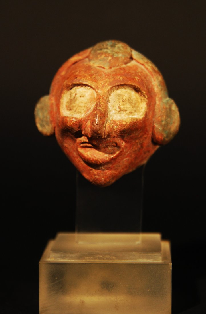 500 B.C. - 1200 A.D. MAYAN POTTERY BELL: a Maya pottery bell pendant depicting a human head, painted red-brown and blue-green. Intact. Mounted on a lucite cube base.Period:Ca. 500 B.C. to 1200 A.D.Size:3-1/4” Provenance:Estate of Mr. and M