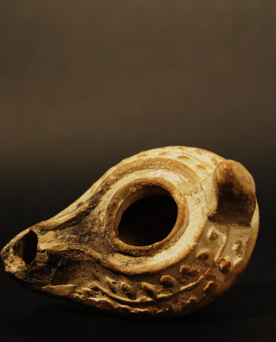 100 A.D. ROMAN OIL LAMP: A Roman oil lamp decorated with a relief leafy branch border. Some ancient loss around the wick hole, otherwise intact. Size: 3 1/4”L. Gerald Nordland collection, Chicago.