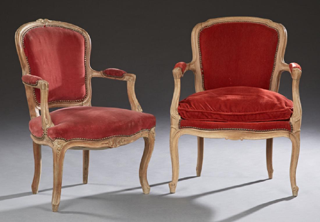 Two French Carved Beech Fauteuils, early 20th c., with: Two French Carved Beech Fauteuils, early 20th c., with shield backs, one with a floral carved crest rail, with upholstered arms and bowed seats, on cabriole legs with toupie feet, in red velvet uphols