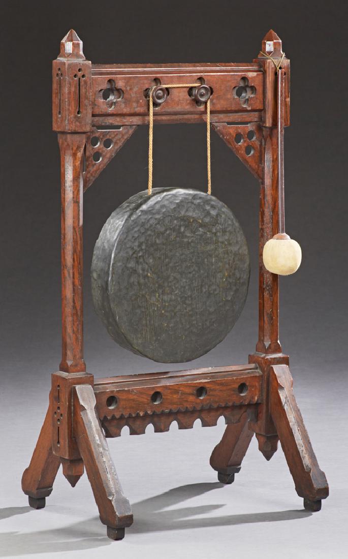 English Carved Mahogany Gothic Style Dinner Gong on: English Carved Mahogany Gothic Style Dinner Gong on Stand, 20th c., with mallet, the circular hammered brass gong suspended within a quartrafoil pierced stand, on a trestle base, H.- 39 1/2 in., W.- 2