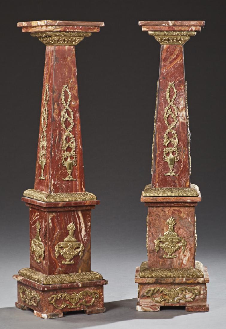 Pair of Neoclassical Ormolu Mounted Rouge Marble: Pair of Neoclassical Ormolu Mounted Rouge Marble Pedestals, 20th c., of tapering forms, the sides mounted with ormolu floral baskets, over ormolu urns to a stepped base, H.- 47 3/4 in., W.- 12 1/2 in.