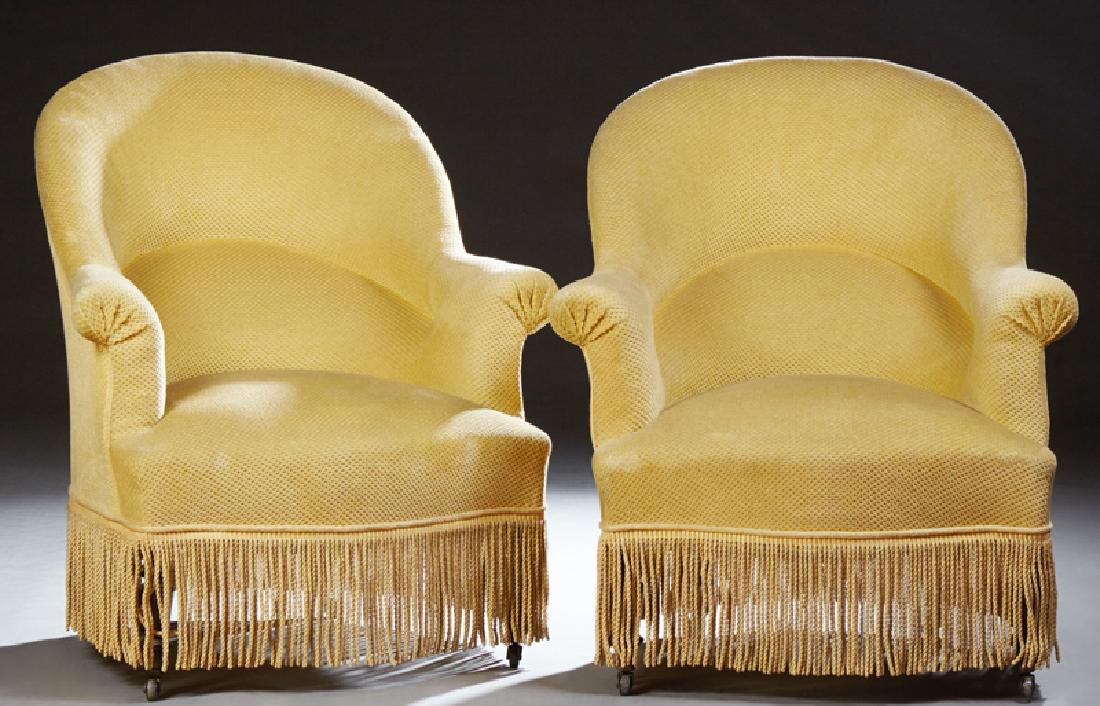 Pair of Upholstered Bergeres, early 20th c., the arched: Pair of Upholstered Bergeres, early 20th c., the arched curved back to splayed rolled arms flanking a bowed seat, on turned tapered legs on casters, in muted gold textured upholstery with a bullion fr