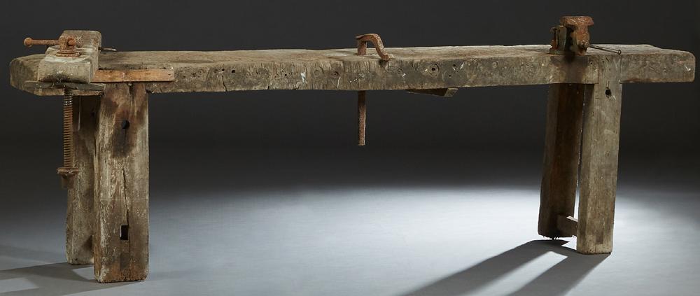French Cabinetmaker: French Cabinetmaker's Carved Elm Workbench, 19th c., the rectangular top with a wood vise, iron wood clamps, and an iron vise, on thick trestle supports, H.- 29 in., W.- 98 1/2 in., D.- 15 1/4 in.