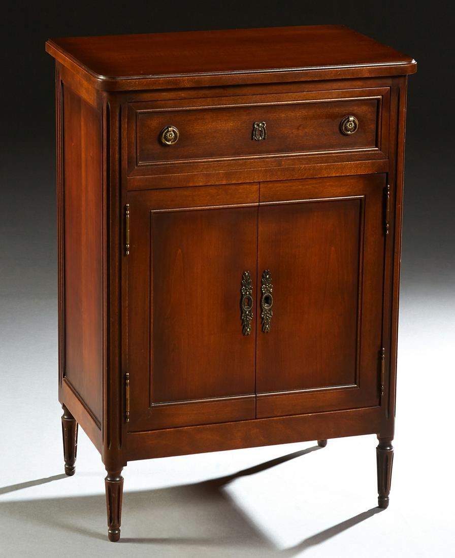 French Provincial Louis XVI Style Carved Cherry: French Provincial Louis XVI Style Carved Cherry Confiturier, 20th c., the ogee edge rounded corner top over a frieze drawer and a double cupboard door, on a plinth base on reeded tapered legs, with ke