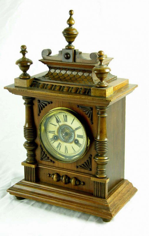 German Carved Birch Mantel Clock, early 20th c., w: German Carved Birch Mantel Clock, early 20th c., with a spindle carved top on a lappet "roof" on a stepped crest, over the face flanked by applied half Columns, on a stepped wooden base, on turned fee