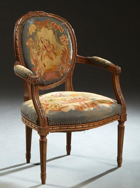 French Carved Walnut Louis XVI Fauteuil, 19th c., the canted medallion back over upholstered reeded: French Carved Walnut Louis XVI Fauteuil, 19th c., the canted medallion back over upholstered reeded arms and a bowed cushion seat, on turned tapered reeded legs with toupie feet, in needlepoint uphols