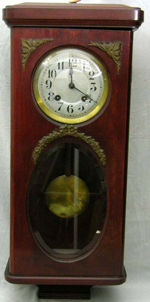 Carved Mahogany Wall Clock, early 20th c., in the: Carved Mahogany Wall Clock, early 20th c., in the Louis XVI style, with ormolu mounts, the lower section of the door with an oval beveled glass plate, time and strike, H.- 30 in., W.- 13 1/2 in., D.-