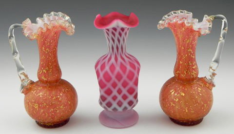 Three Pieces of Art Glass, early 20th c., a pair o: Three Pieces of Art Glass, early 20th c., a pair of orange cased glass ewers with scalloped rims and applied clear handles, together with a pink and with quilted pinched vase. (3 Pcs.)