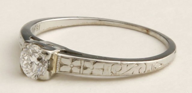 18K White Gold Diamond Solitaire Ring, with a cent: 18K White Gold Diamond Solitaire Ring, with a central 15 point round diamond, the sides of the band with relief decoration, size- 5 1/4.