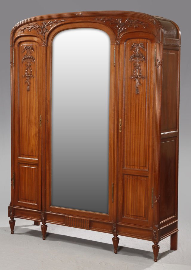 Carved Mahogany Triple Door Armoire, c. 1920, the arche: Carved Mahogany Triple Door Armoire, c. 1920, the arched top with a reeded and crossed ribbon border over relief leaf and branch carving, above a central wide beveled mirror door, flanked by narrow do