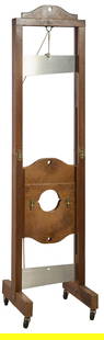 Magic Trick Iron and Wood Guillotine, 20th c., H.- 76 in., W.- 19 in., D.- 20 in.: Magic Trick Iron and Wood Guillotine, 20th c., the tall stockade with a channel hung angled blade, above a lower arrangement to hold head and neck in place, on a trestle form base on casters, H.- 76