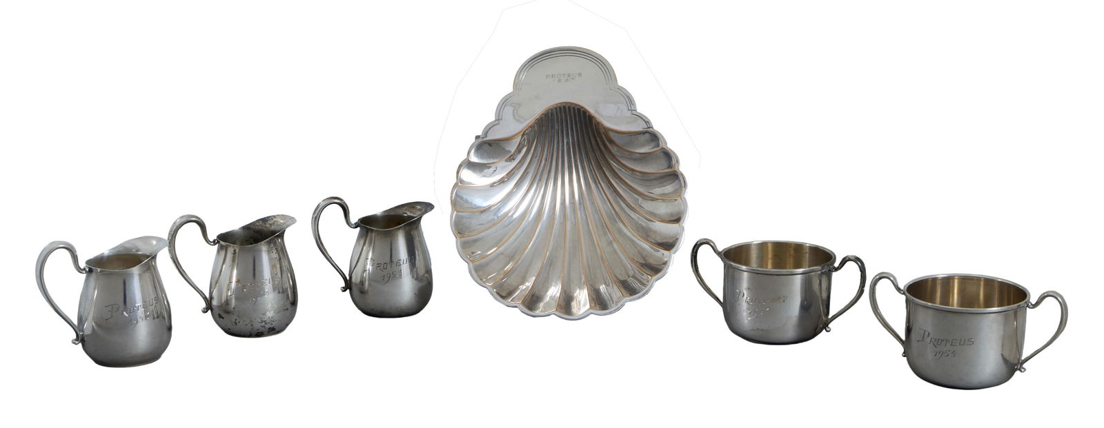 Six Mardi Gras Krewe Favors, Krewe of Proteus, 20th c., Total Sterling Wt.- 6.30 Troy oz.; 1947- H.-: Six Mardi Gras Krewe Favors, Krewe of Proteus, 20th c., consisting of a 1947 example of a silverplate card tray in the form of a scallop shell, by International Silver Co., number 676; three 1953 exam