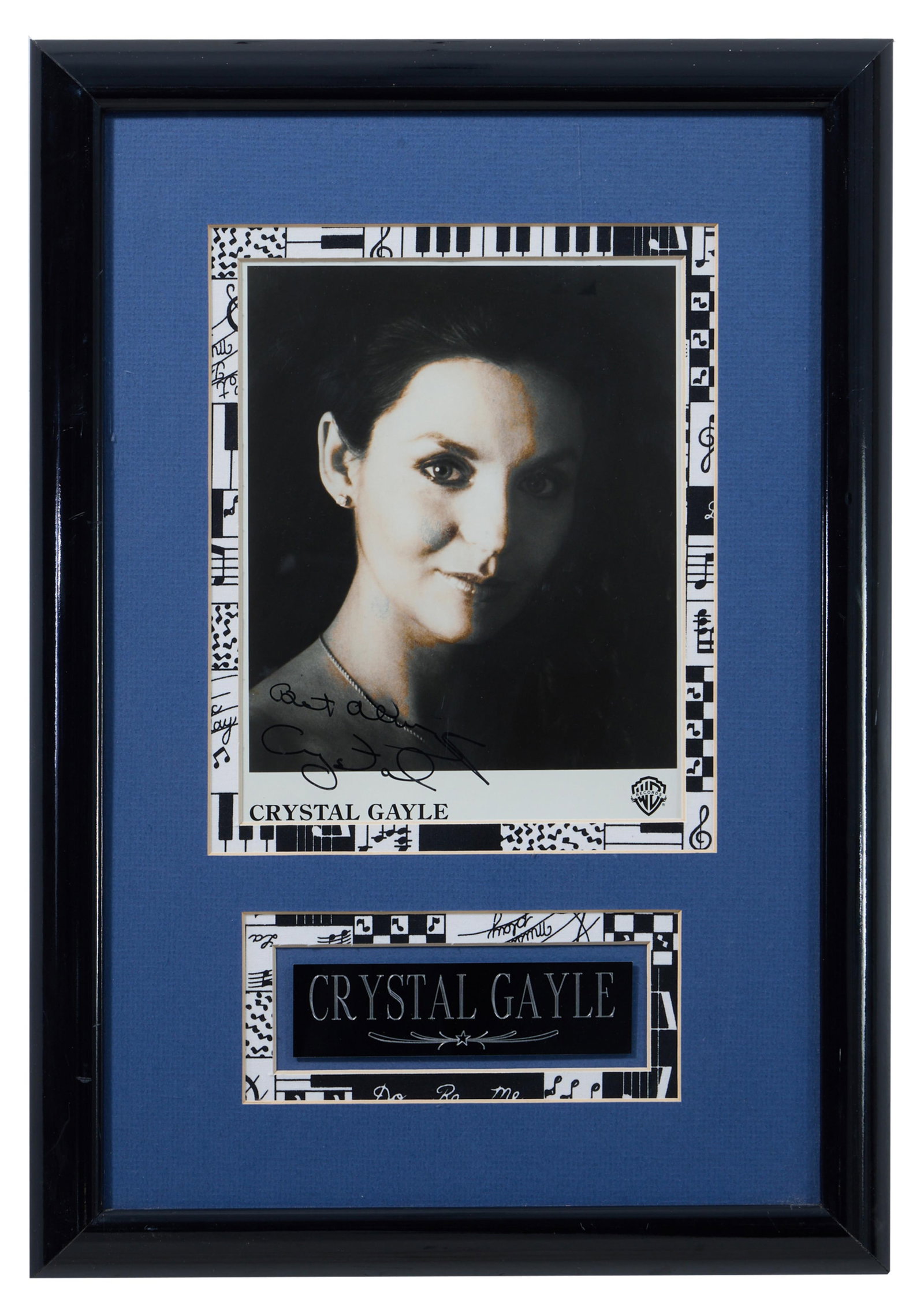 Crystal Gayle Autographed Memorabilia, Overall- H.- 20 in., W.- 14 in.: Crystal Gayle Autographed Memorabilia, with signed Warner Bros. headshot and name plaque, in a black frame with plexiglass, Overall- H.- 20 in., W.- 14 in. Provenance: The Estate of Joseph A. Jaeger, 