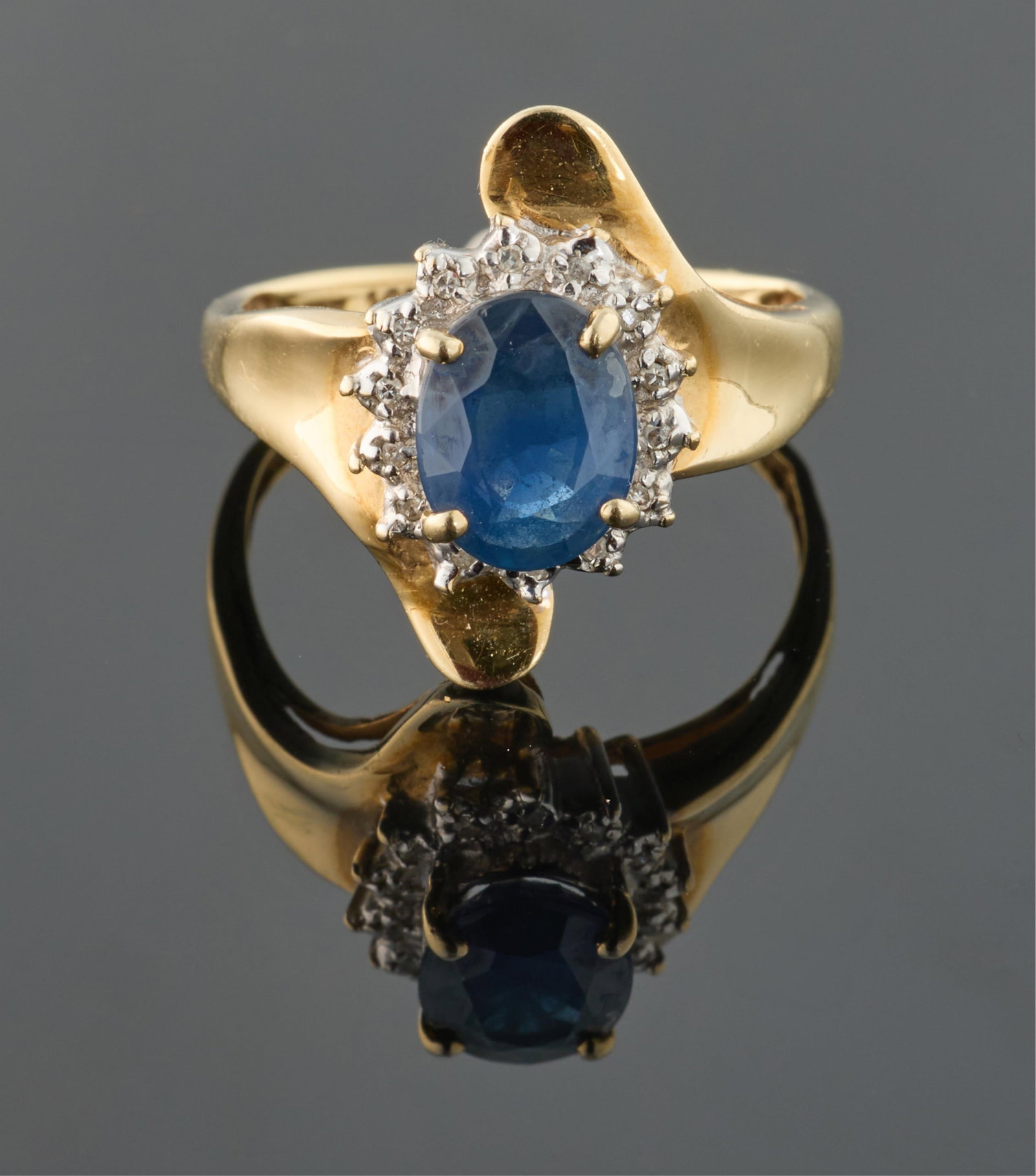 Ladies' 14K Two Tone Gold Sapphire and Diamond Ring, Size- 8.: Ladies' 14K Two Tone Gold Sapphire and Diamond Ring, the center mounted oval blue sapphire atop a border of tiny round white diamonds over the swirled shoulders of the band, Size- 8. Please Note: All 