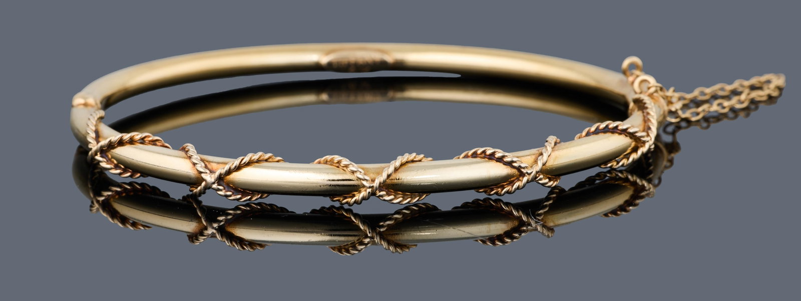 14K Yellow Gold Hinged Bangle, App. Total Wt.- 10 grams, Int. H.- 1 7/8 in., Int. W.- 2 1/4 in.: 14K Yellow Gold Hinged Bangle, with twisted rope applique, marked "TIFFANY 14K", with safety chain, App. Total Wt.- 10 grams, Int. H.- 1 7/8 in., Int. W.- 2 1/4 in. Please Note: All assessments of gem