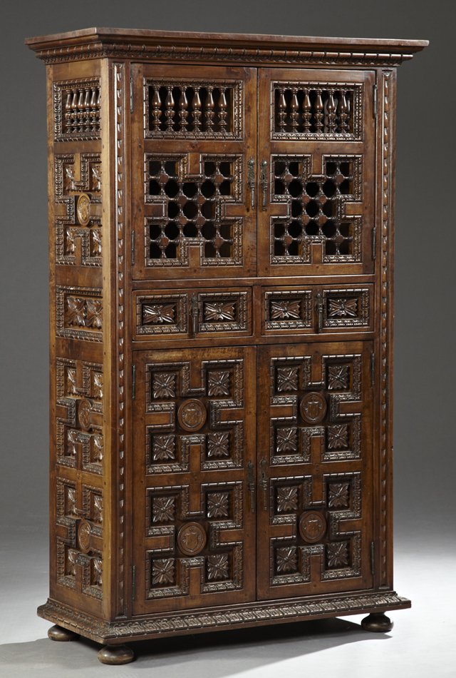 Spanish Carved Walnut Cabinet, 20th c., with a stepped: Spanish Carved Walnut Cabinet, 20th c., with a stepped carved ogee top over a cupboard with turned spindled doors and sides over a leaf carved frieze drawer above a large lower cupboard with leaf carv