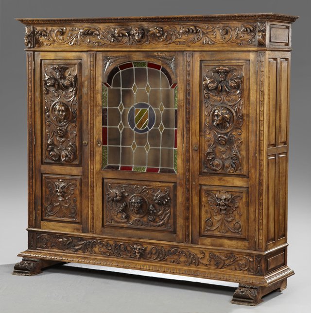 Spanish Highly Carved Birch Renaissance Style Bookcase,: Spanish Highly Carved Birch Renaissance Style Bookcase, 20th c., with a carved ogee crown over a high relief carved frieze with a central head, above a center door with an upper leaded glass panel ove