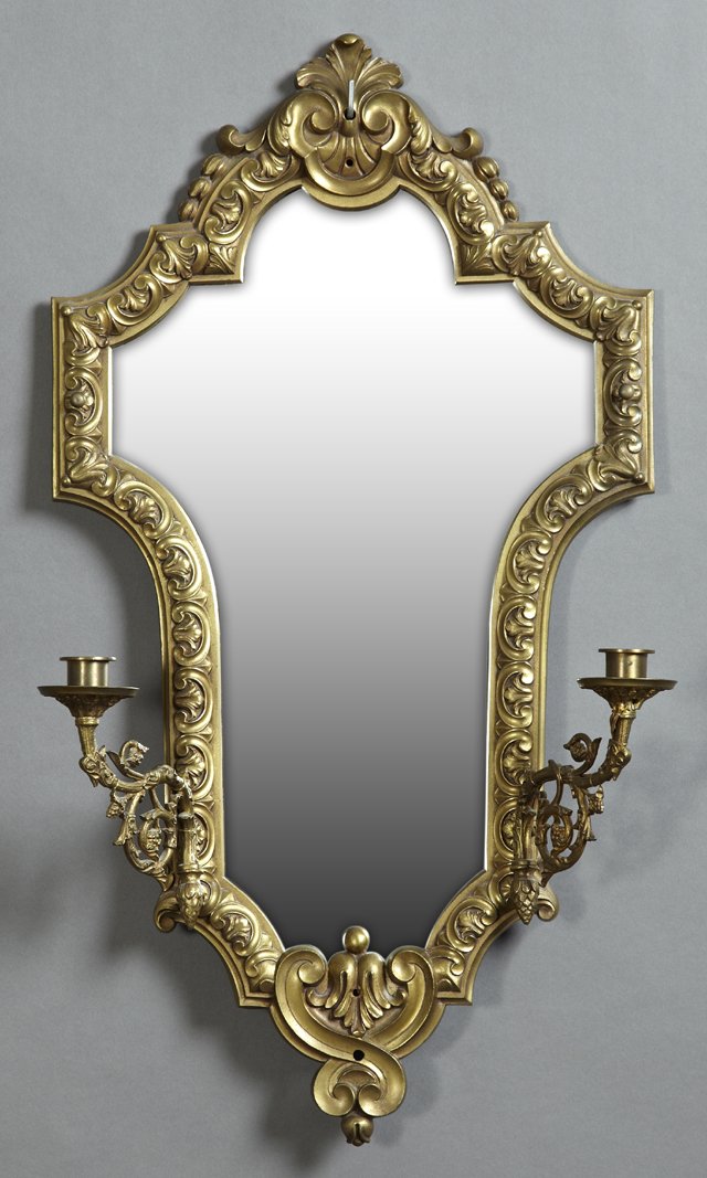 Brass Two Light Mirror Sconce, 20th c., the shield: Brass Two Light Mirror Sconce, 20th c., the shield shaped mirror with a relief leaf and scroll frame, the sides with two scrolled candle arms, not electrified, H.- 25 in., W.- 14 1/8 in., D.- 5 in.
