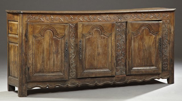 French Provincial Carved Oak Sideboard, 19th c., the: French Provincial Carved Oak Sideboard, 19th c., the stepped rounded edge top over a frieze with relief flowers and tendrils, above three fielded panel doors, separated by arched flower and tendril ca