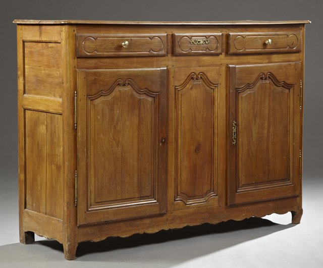 French Provincial Carved Walnut Sideboard, 19th c., the: French Provincial Carved Walnut Sideboard, 19th c., the rounded corner ogee edge top over three frieze drawers above double arched fielded panel cupboard doors separated by an arched fielded panel, on