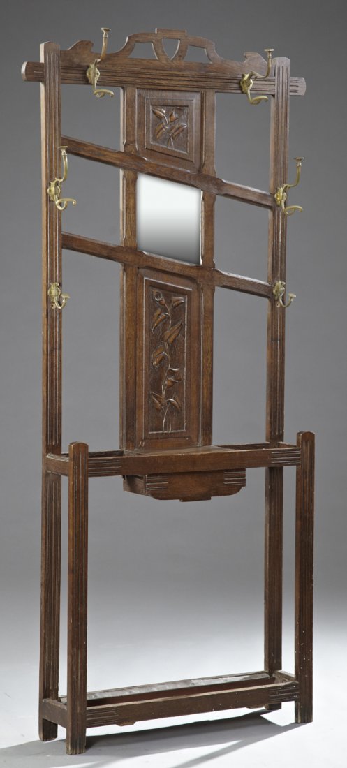 Art Nouveau Carved Oak Hall Stand, c. 1900, with a: Art Nouveau Carved Oak Hall Stand, c. 1900, with a pierced crest over a back with central carved leaf panels over a beveled mirror, above a center drawer flanked by umbrella racks over an iron drip tr