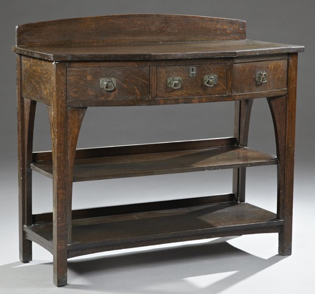American Mission Oak Server, c. 1910, stamped Limbert,: American Mission Oak Server, c. 1910, stamped Limbert, the arched back splash over a geometric top with a bowed front with three frieze drawers over two shelves, the whole on square block legs, matchi