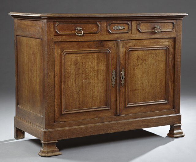 French Provincial Carved Oak Sideboard, c. 1850, the: French Provincial Carved Oak Sideboard, c. 1850, the rounded edge canted corner top over three frieze drawers and double arched panel cupboard doors, on a stepped plinth base, on ogee stepped block fe