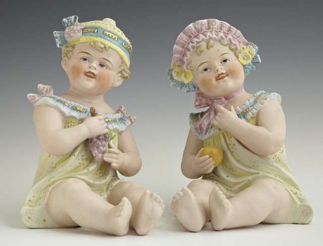 Pair of German Polychromed Bisque Piano Babies, late: Pair of German Polychromed Bisque Piano Babies, late 19th c., one holding an apple, the other holding grapes, H.- 7 1/2 in., W.- 5 1/4 in., D.- 6 in.