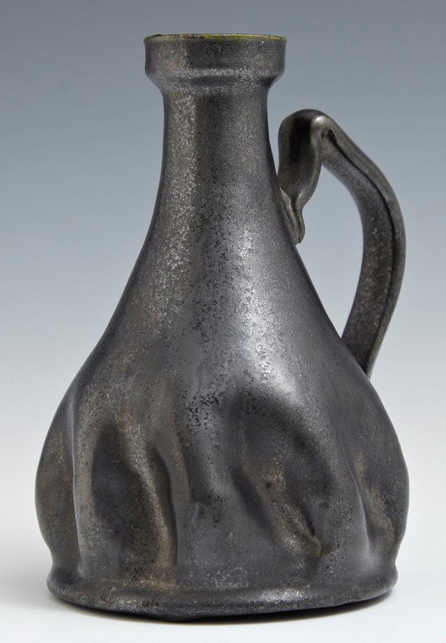 George Ohr Pottery Candlestick, in gunmetal glaze, of: George Ohr Pottery Candlestick, in gunmetal glaze, of pitcher form with a crimped edge and an open bottom, with an inscribed signature on the inside bottom edge, G E Ohr, H.- 5 1/4 in., W.- 4 in., D.-