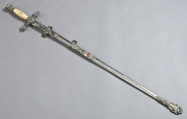 Knights of Columbus Ceremonial Sword, early 20th c., by: Knights of Columbus Ceremonial Sword, early 20th c., by the Pettigrew Bros. Mfg. Co., Cincinnati, the blade engraved "Irvin Jackson," with a celluloid handle and an enamel and relief decorated scabbar