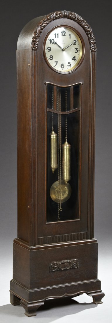 German Junghans Tall Case Clock, c. 1900, retailed by: German Junghans Tall Case Clock, c. 1900, retailed by Wempe, the arched crown over a brass and steel dial, two brass weights and a pendulum, on a stepped base with applied floral decoration, on ogee b