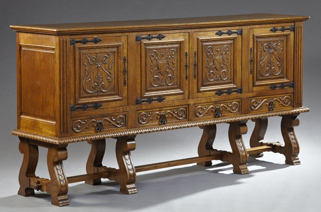 Spanish Carved Oak Sideboard, 20th c., the stepped ogee: Spanish Carved Oak Sideboard, 20th c., the stepped ogee edge rectangular top over four floral relief carved cupboard doors with wrought iron strap hinges and escutcheons, over lower drawers on four ca