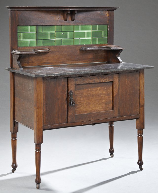 English Arts and Crafts Carved Oak Marble Top: English Arts and Crafts Carved Oak Marble Top Washstand, c. 1910, the green ceramic tiled backsplash with two candle stands, over a figured black marble on a base with a single cupboard door, on turne