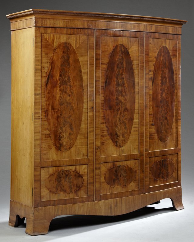 English Edwardian Inlaid Mahogany Triple Door Bowfront: English Edwardian Inlaid Mahogany Triple Door Bowfront Armoire, early 20th c., the dentillated cavetto crown over three oval medallion inlaid doors, the whole on splayed bracket feet joined by an arch