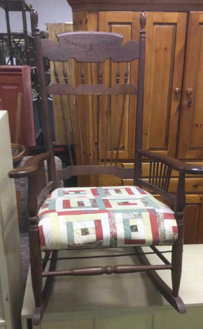 Aantique Carved Wooden Cushioned Rocking Chair: Antique Carved Wooden Cushioned Rocking Chair, Contains attached cushion with multi toned design detail, Cushion is patchwork quilt, spindle back, spindle armrests, caarved wide arms, and carved leaf 