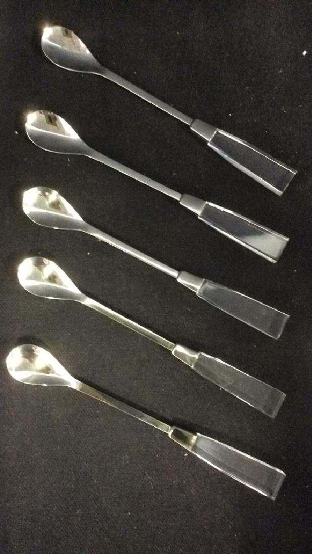 Lot 5 SUPREME CUTLERY Lucite Handled Spoons: Spoons are silver toned, appear to be stainless steel. Handles are lucite. Includes original box. Box is black toned and reads SUPREME CUTLERY. Each piece measures approx 9 inches long.