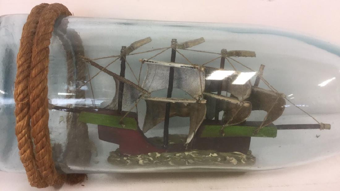 Ship In A Glass Bottle Sculpture: Ship In A Glass Bottle Sculpture. A 1800 ml light blue glass bottle with rope on the base and neck and miniature four sailed ship on the inside. Light surface scratches to bottle. Measures approx 16 i