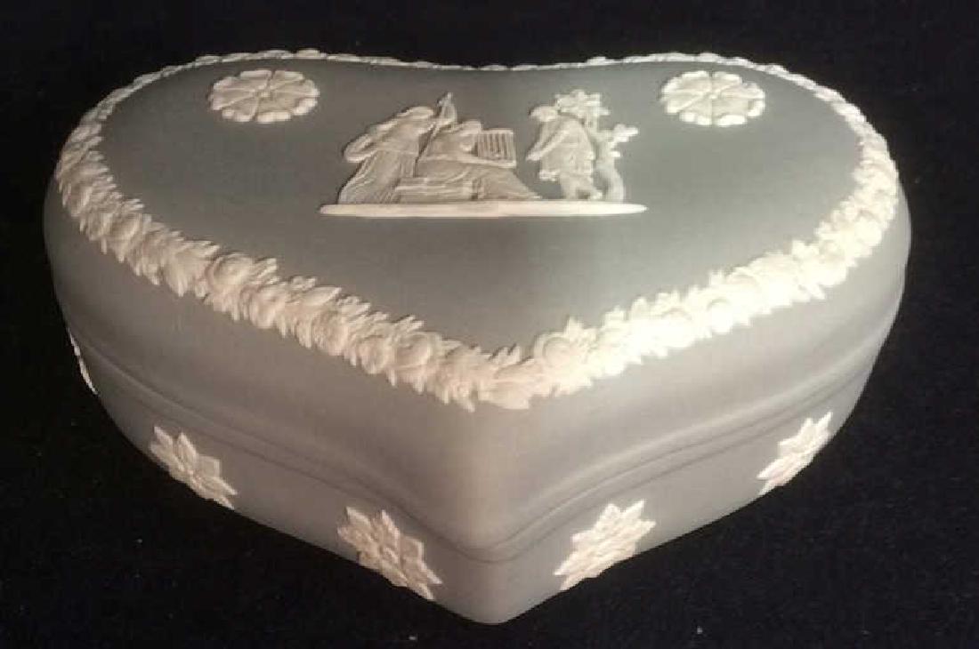WEDGWOOD Heart Shaped Jewelry Box: Jewelry box is grey toned. Box is heart shaped. Marked WEDGWOOD MADE IN ENGLAND on underside. Contains intricate white toned floral and figural detail. Measures approx 5.5inches long 4 inches deep 1.5