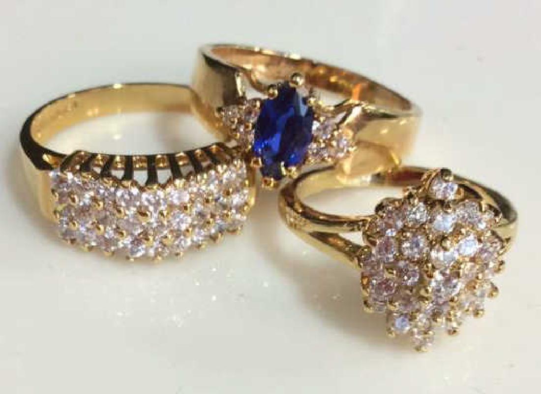 Lot 3 Rhinestone & Gold Plated Rings: Lot 3 Rhinestone & Gold Plated Rings. One ring with oval cut blue toned rhinestone framed on both sides by three round cut colorless rhinestones, marked as S 14 K HGE LIND. One unmarked ring, costume 