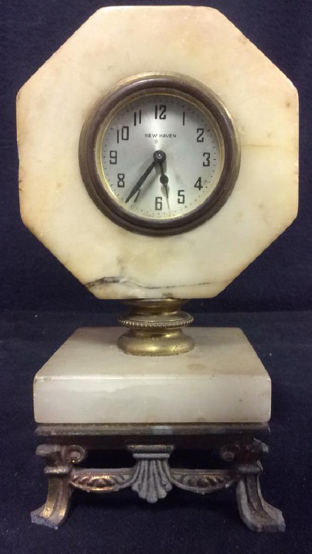 Pedestaled NEW HAVEN Octagon Alabaster Clock: Marked NEW HAVEN MADE IN USA on clock face. Clock is Octagon shaped, base is square shaped. Contains ornate gold toned detail on bottom of base. 2 of the feet are chipped. Measures approx 7.5 inches t