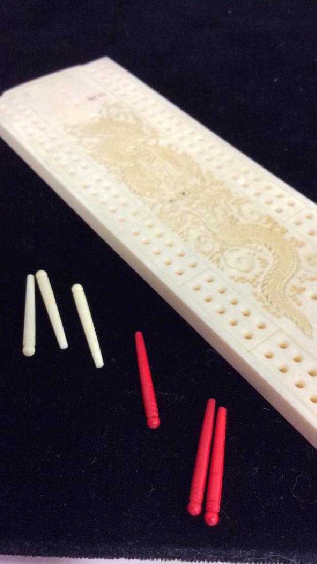 Vintage Carve Bone Cribbage Game: Vintage Carve Bone Cribbage Game. Bone panel with hidden storage holding three red toned pins and three beige toned pins. Top of game board has carved twisted dragon design. Measures approx 6 in tall 