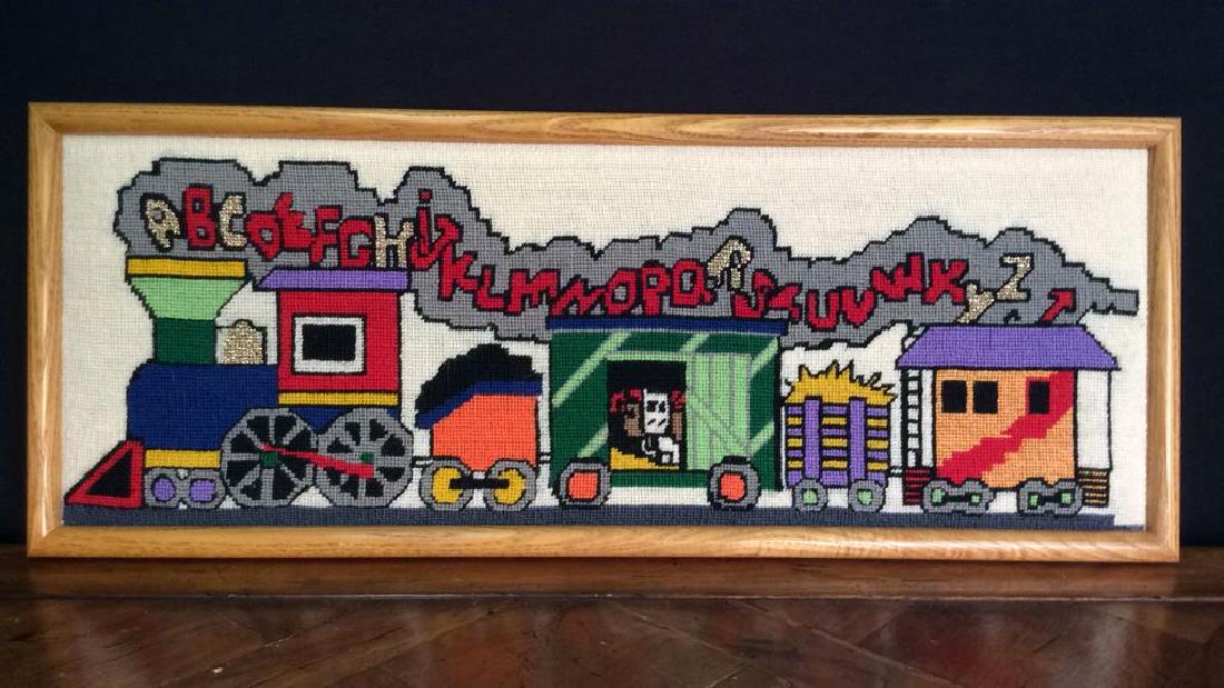 Framed Alphabetical Train Needlepoint: Professionally framed with wooden frame. Depicts a multi toned train emitting smoke with the letters of the alphabet. Measures approx 25 inches long 10 inches tall
